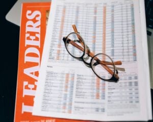 Glasses resting on a financial report filled with numbers, next to an orange 'LEADERS' magazine cover.