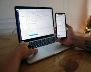 Person using a laptop and a smartphone to monitor stock trading charts and data on the screen and phone edge-to-edge.