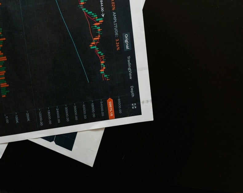 Tilted printed dark chart with multiple colorful line graphs and an orange data badge along the right edge; labels such as Original and TrainView visible, placed on white paper atop a dark surface.