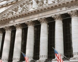 Front facade of the New York Stock Exchange with tall classical columns and American flags