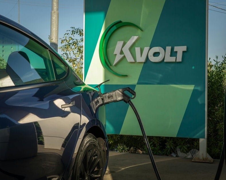 Electric car plugged into a charging station with a bold KVolt sign in the background.