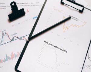 Clipboard with financial charts and a pencil, showing Dow Jones values in 2020 and stock trends across months.
