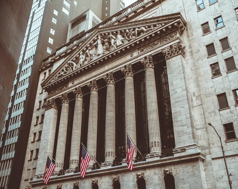 Classical stone building with tall columns and a decorative pediment, American flags waving outside.