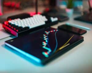 Tablet on a desk showing a colorful stock chart; a keyboard and smartphone nearby.