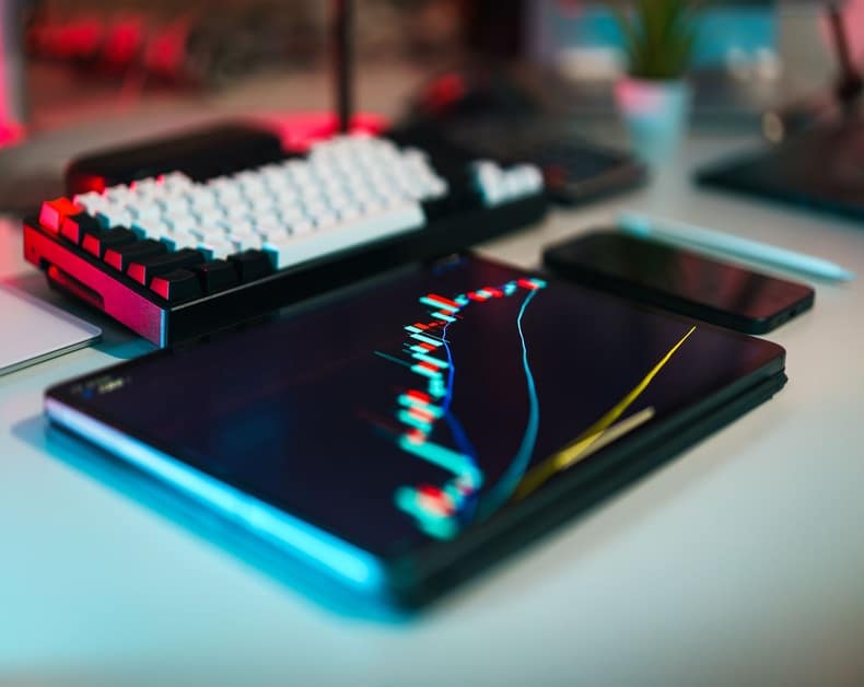 Tablet on a desk showing a colorful stock chart; a keyboard and smartphone nearby.
