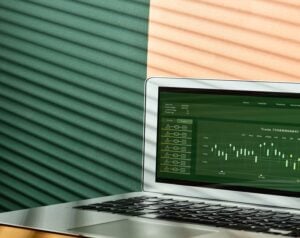Laptop displaying a green stock market trading chart on the screen with candlestick visuals and data panels