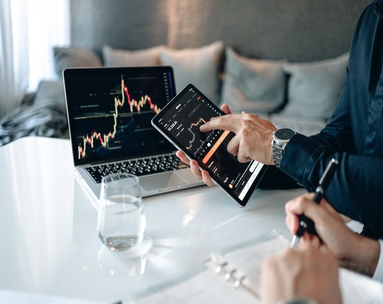 Trader reviews stock trades on tablet and laptop with candlestick charts on screen