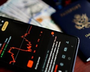 Smartphone screen showing a red line graph on a financial app, with cash and a blue passport in the background.