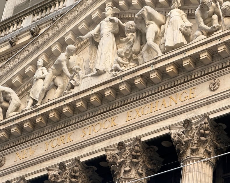 Facade of the New York Stock Exchange with statues and the gold-lettered inscription 'New York Stock Exchange'.