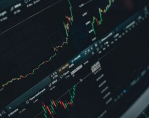 Stock trading dashboard with candlestick charts showing rising prices (green candles) and data on a monitor.