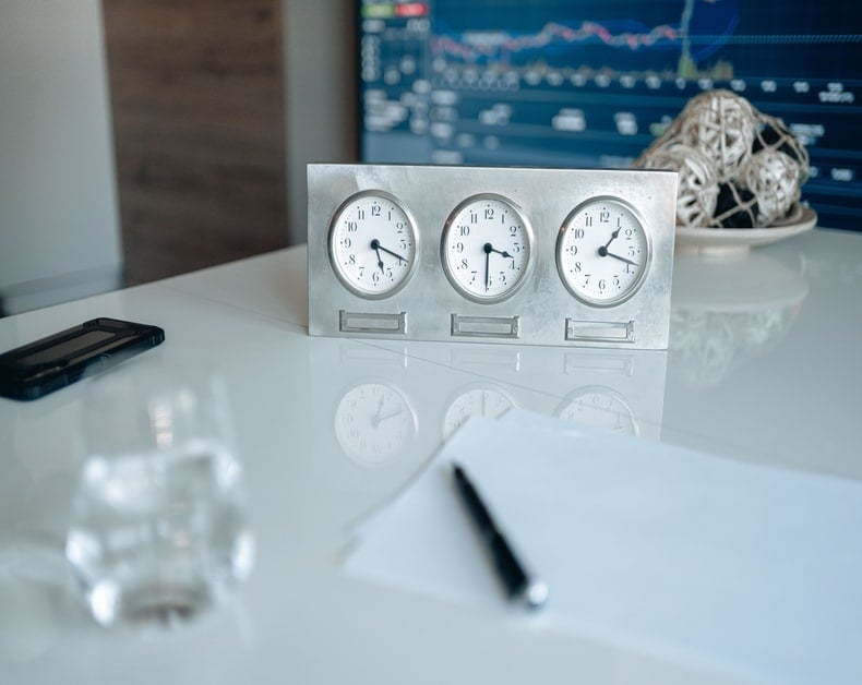 Triple clock desk ornament showing different times on a metal frame, with a pen and paper in the foreground.