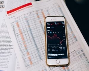 Newspaper page labeled 'Economic & financial indicators' with a smartphone showing a stock chart laid on top.