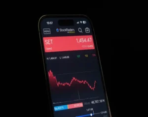 Smartphone screen showing a stock trading app with SET index at 1,454.47 and a red price banner above a fluctuating chart.