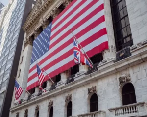 A grand stone building with a giant American flag draped across its façade and several smaller flags along the balcony railings.