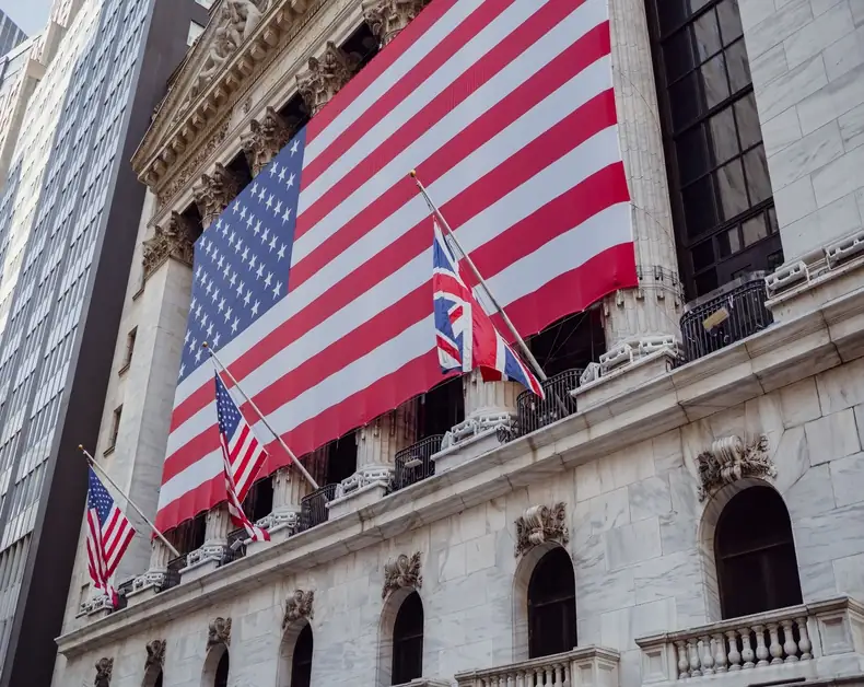 A grand stone building with a giant American flag draped across its façade and several smaller flags along the balcony railings.